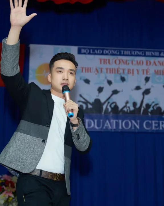 Sang Le on stage with a microphone, speaking to an audience